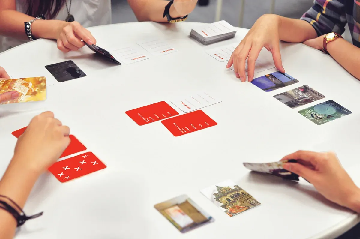 Four people playing with the _ING deck: red ring-suit cards and photo cards of British and Indian life