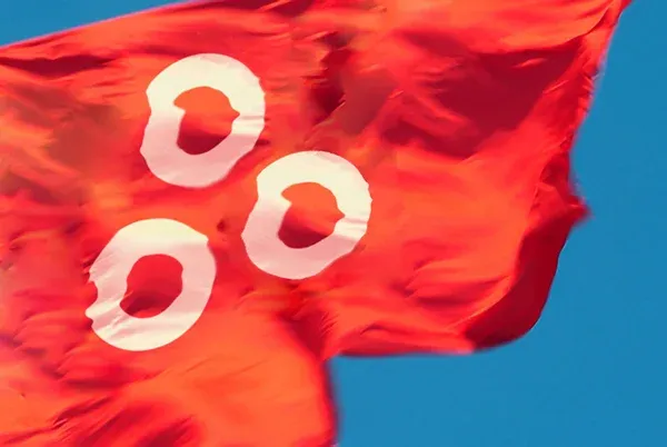 A red flag printed with three white rings, waving against a blue sky